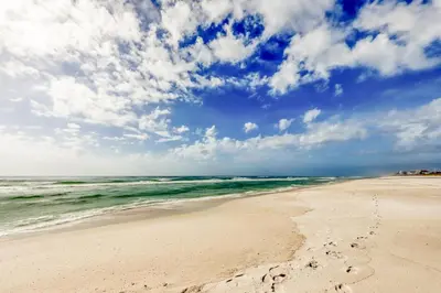 a beach with footprints in the sand and the ocean at Gulf-front condo with bicycles lazy river & pickleball in Seacrest