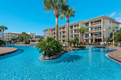 a swimming pool with palm trees in front of a building at Elegant getaway with stunning view lagoon pool & pickleball - close to shops in Seacrest