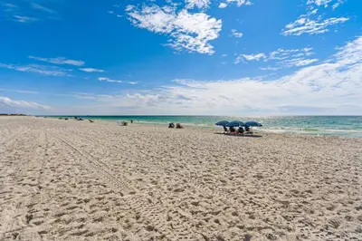 a beach with people sitting under umbrellas and the ocean at Gulf-front view & spacious condo with wraparound balcony & pickleball in Santa Rosa Beach