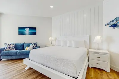 a white bedroom with a bed and a blue couch at Gulf-front view & spacious condo with wraparound balcony & pickleball in Santa Rosa Beach