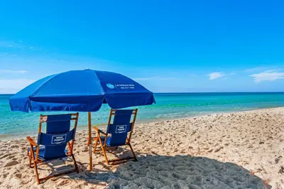 two chairs and an umbrella on a beach at Beach dwelling with great view pool & pickleball - snowbird-friendly in Seacrest