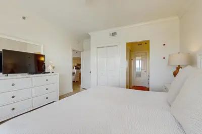 a white bedroom with a large bed and a flat screen tv at Condo on the beach with tennis pickleball shuffleboard & balcony in Seacrest