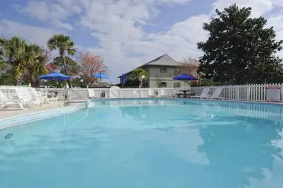 a large blue swimming pool with chairs and umbrellas at Cute ground floor condo with shared pool access to shuffleboard and tennis in Santa Rosa Beach