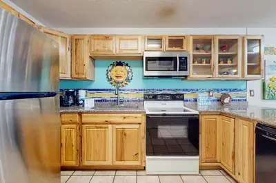 a kitchen with wooden cabinets and a refrigerator at Cute ground floor condo with shared pool access to shuffleboard and tennis in Santa Rosa Beach