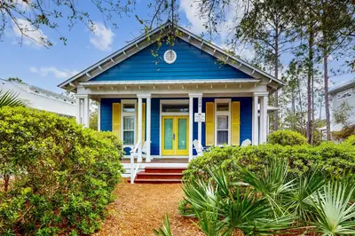 a blue and yellow house with two white chairs at Colorful house near the beach with shared swimming pool in Santa Rosa Beach