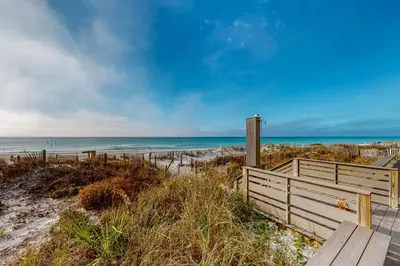 a wooden bench sitting on a beach near the ocean at Lovely first floor condo with ocean views patio & grill - steps from the beach in Santa Rosa Beach