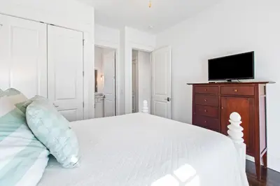 a white bedroom with a bed and a tv on a dresser at Seagrove Serenity 4BR Coastal Retreat with Pool & Bikes in Santa Rosa Beach