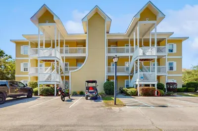 a large yellow building with a scooter parked in a parking lot at Pool-view condo with private balcony AC & washer&dryer in Santa Rosa Beach