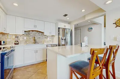 a kitchen with white cabinets and a counter and chairs at Gulf front condo with beach access pool hot tub tennis & pickleball in Seacrest