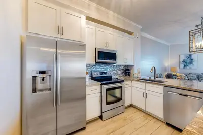 a kitchen with white cabinets and a stainless steel refrigerator at Stunning 4th-floor condo with pool tennis pickleball ocean & beach view in Santa Rosa Beach