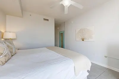a bedroom with a white bed with a ceiling fan at Ground floor beachfront condo with shared pool and beach access in Santa Rosa Beach