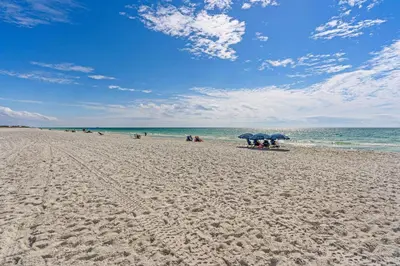 a beach with people sitting under umbrellas and the ocean at Ground floor beachfront condo with shared pool and beach access in Santa Rosa Beach