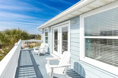 a white house with two chairs on a porch at New Kululu WEST- 3 BR, Sleeps 11, Heated Salt Water Pool, Bikes & moments from the beach in Santa Rosa Beach