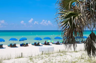 a beach with chairs and blue umbrellas and the ocean at Bikini Beach Resort in Panama City Beach