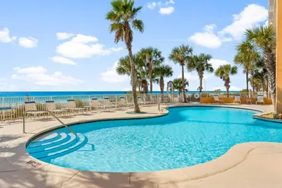 a swimming pool with palm trees and the ocean at Splash Beach Resort by Panhandle Getaways in Panama City Beach