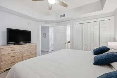 a white bedroom with a bed and a flat screen tv at Calypso 2-1907 West in Panama City Beach