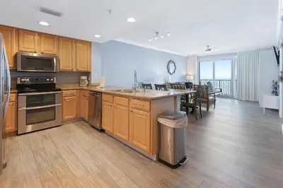 a kitchen with wooden cabinets and a dining room with a table at Grandview East 1203 in Panama City Beach
