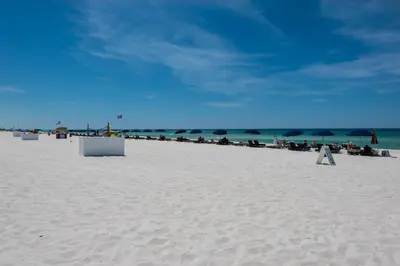 a sandy beach with people sitting under umbrellas at Origin at Seahaven 825 in Panama City Beach
