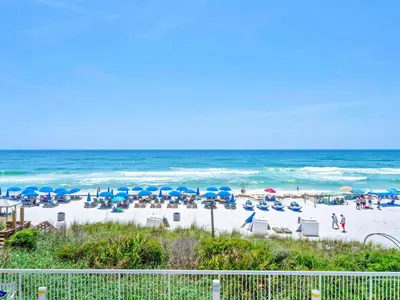 a beach with chairs and blue umbrellas and the ocean at Seychelles 207 in Panama City Beach