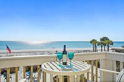 a table with two wine glasses on a balcony with the beach at Beachside West Townhome in Panama City Beach