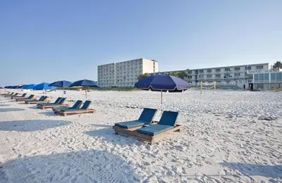 a row of lounge chairs and an umbrella on a beach at Beachside West Townhome in Panama City Beach