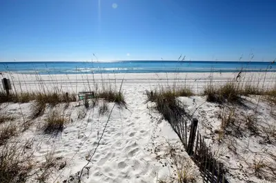 a beach with sand and grass and the ocean at Beachside West Townhome in Panama City Beach