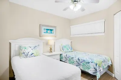 a white bedroom with two beds and a window at Aquavista 304W in Panama City Beach