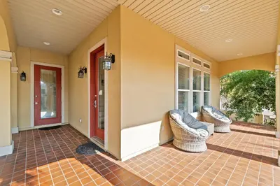 a porch with two wicker chairs and a red door at La Valencia Villas in Rosemary Beach
