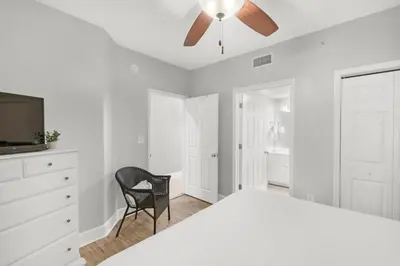 a white bedroom with a ceiling fan and a chair at Majestic Beach Towers 1-1006 in Panama City Beach