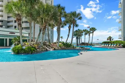 a swimming pool with palm trees in front of a building at Long Beach Resort by Panhandle Getaways in Panama City Beach