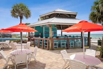 a group of tables and chairs with red umbrellas at Beachcomber Beachfront Hotel, a By The Sea Resort in Panama City Beach