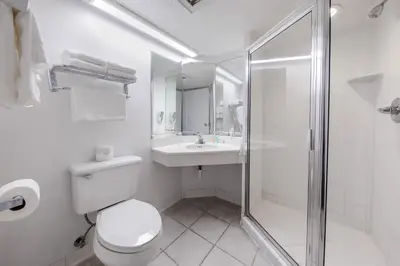 a white bathroom with a toilet and a shower at Beachcomber Beachfront Hotel, a By The Sea Resort in Panama City Beach