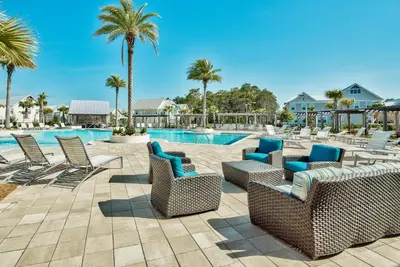 a patio with chairs and a swimming pool with palm trees at Prominence on 30A by Panhandle Getaways in Watersound Beach