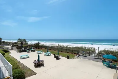a patio with tables and benches and the beach at Mariner West 205 in Panama City Beach