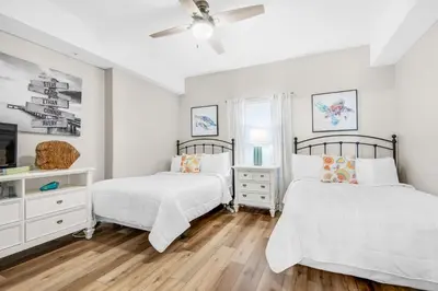 two beds in a bedroom with white walls and wood floors at Ocean Reef 1708 in Panama City Beach