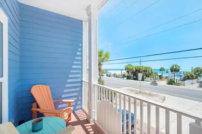 a blue house with a rocking chair and a balcony with a view at Vista del Mar I Rest-A-While 201 in Panama City Beach