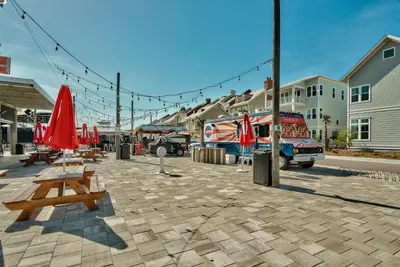 a patio with tables and red umbrellas on a street at Prominence Rentals on 30A by Panhandle Getaways in Watersound Beach