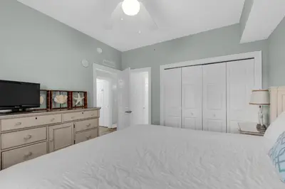 a white bedroom with a large bed and a tv at Calypso 1-608 East in Panama City Beach