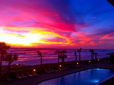 a sunset at the beach with a pool and chairs at Stylish Oceanfront Condo with Beach and Picnic Area Access - Unit 1706 in Panama City Beach