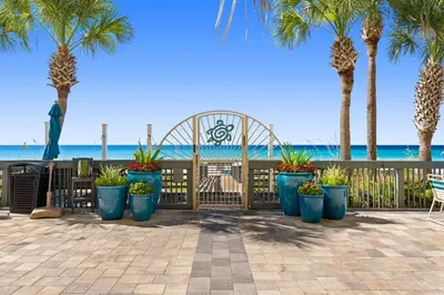 a patio with palm trees and a fence with plants at Beautiful Condo with Spacious Balcony to Enjoy Fascinating Ocean View - Unit 1002 in Panama City Beach