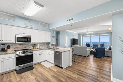 a kitchen with white cabinets and a living room at Beautiful Condo with Spacious Balcony to Enjoy Fascinating Ocean View - Unit 1002 in Panama City Beach