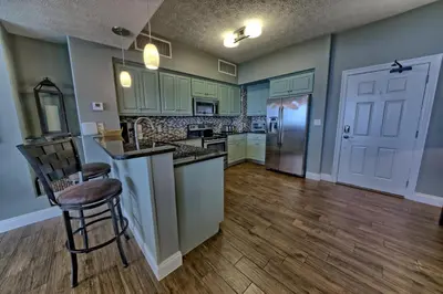 a kitchen with green cabinets and a wooden floor at Pleasant Oceanfront Condo with Large Balcony and Beach Access - Unit 1605 in Panama City Beach