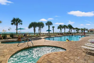 a pool at a resort with palm trees and the ocean at Stunning 16th Floor Condo with Fitness Center, Hot Tubs, Pools, and Beach Access - Unit 1606 in Panama City Beach