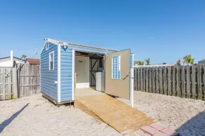 a blue tiny house on the beach next to a fence at Villa Paradise, Pet Friendly in Panama City Beach