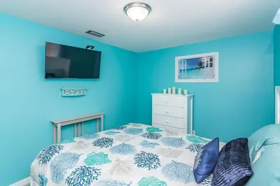 a blue bedroom with a bed and a tv at Villa Serenity, Pet Friendly in Panama City Beach