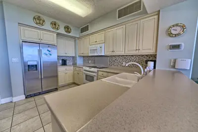 a kitchen with white cabinets and a stainless steel refrigerator at Tropical Gulf Front Condo with Picnic Area & Grills - Unit 0802 in Panama City Beach