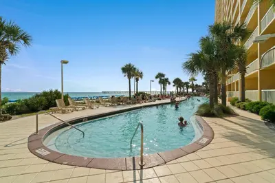 a swimming pool at a resort with palm trees and the ocean at Calypso Beach Resort in Panama City Beach