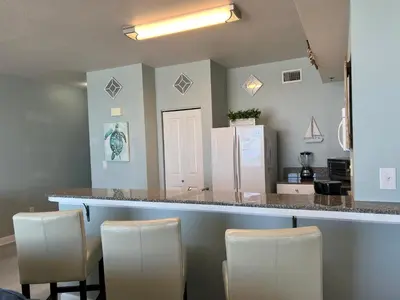 a kitchen with a counter with chairs and a counter top at Shores of Panama Condo With Same Level Parking in Panama City Beach