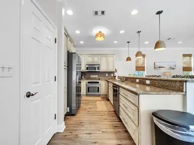 a kitchen with white cabinets and a wooden floor at Aweigh From Home in Santa Rosa Beach