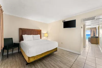 a bedroom with a bed and a television and a chair at Seahaven Beach Hotel Panama City Beach in Panama City Beach